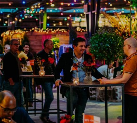 Gasten in gesprek aan statafels onder sfeerverlichting bij Hart van Holland
